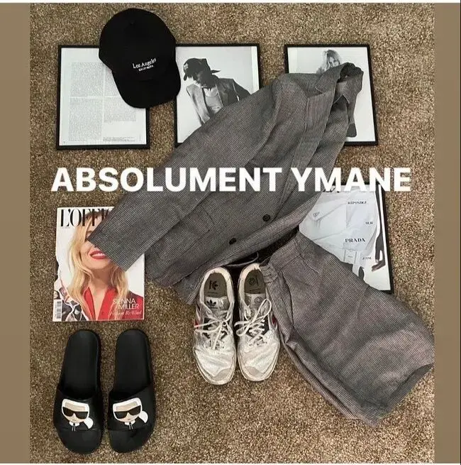 Tenue composée d’un costume gris, de baskets blanches, de claquettes noires et d’accessoires, présentée en flatlay sur un sol beige
