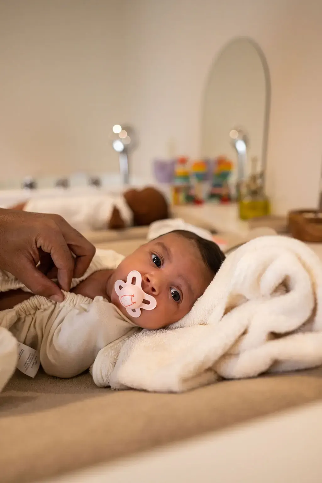 Bébé allongé sur une table à langer, emmitouflé dans une couverture, recevant un soin avec une tétine dans la bouche