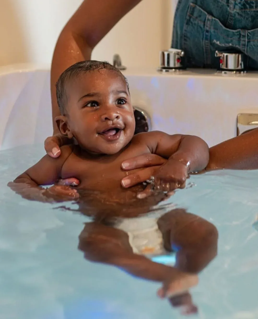 Bébé souriant maintenu délicatement dans un bain d’eau chaude lors d’une séance d’accompagnement au spa