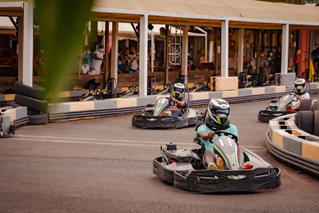Plusieurs personnes conduisant des karts sur un circuit extérieur, avec des spectateurs en arrière-plan