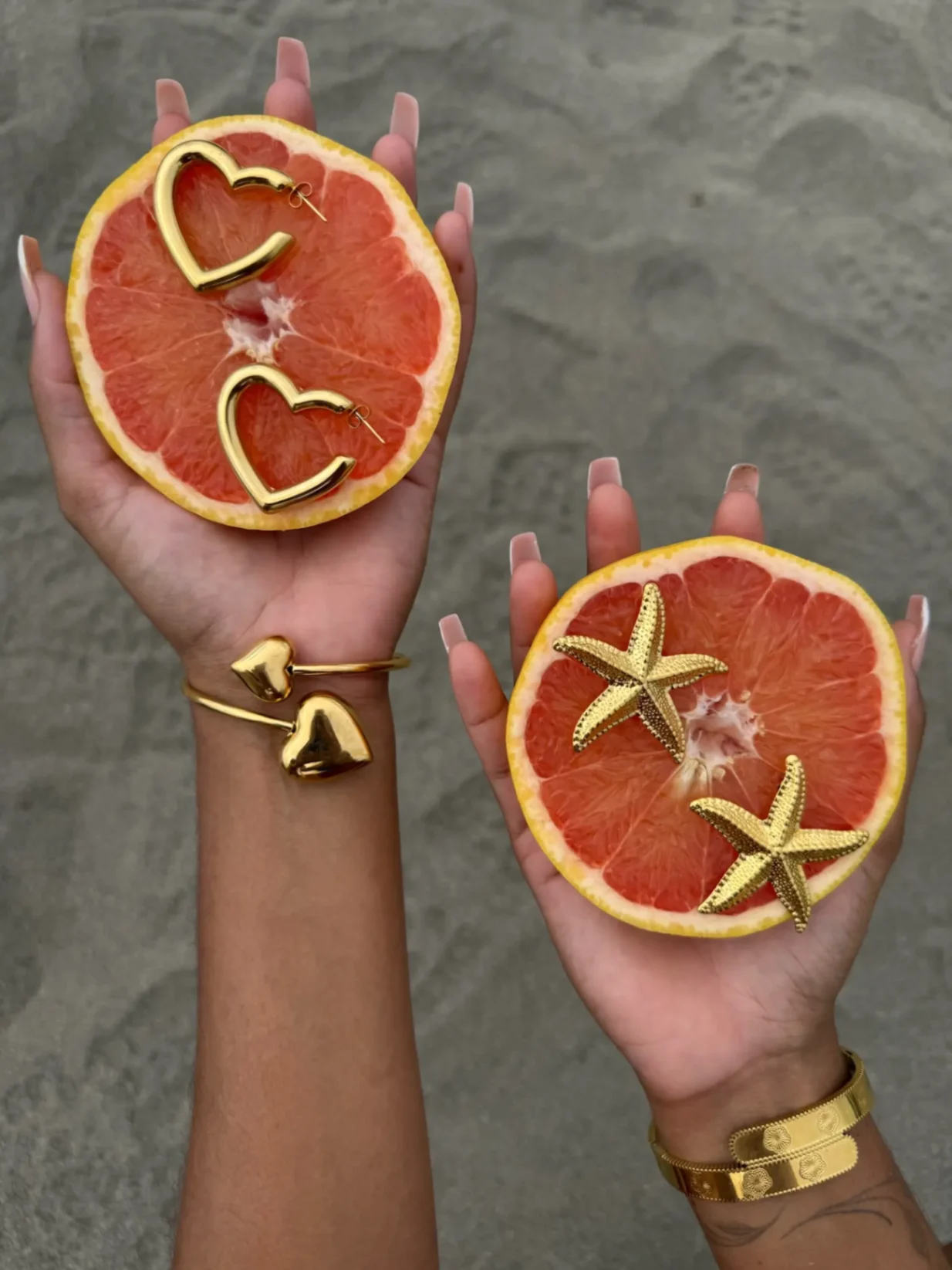Bijoux dorés, dont des anneaux en forme de cœur et des étoiles de mer, disposés sur deux moitiés de pamplemousse tenues dans les mains