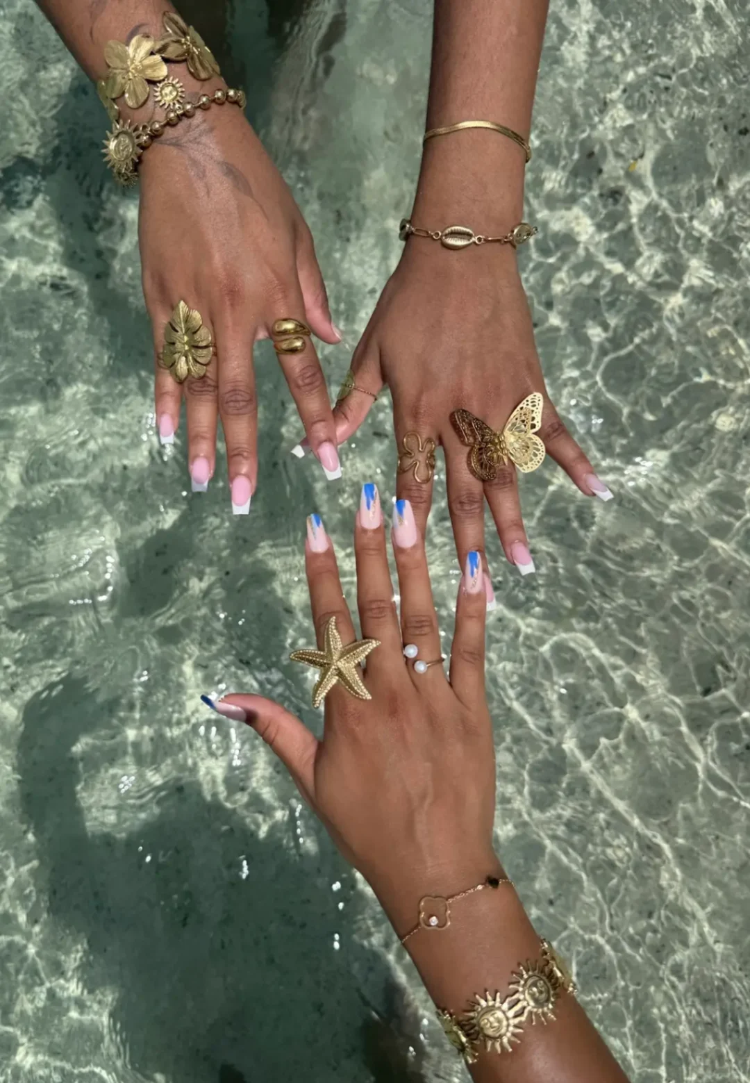 Trois mains ornées de bagues et bracelets dorés posées au-dessus d’une eau claire