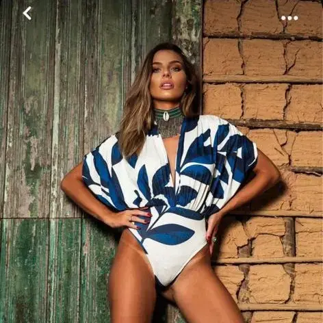 Femme posant devant un mur ancien en portant un maillot une pièce blanc à motifs bleus, style chic et estival
