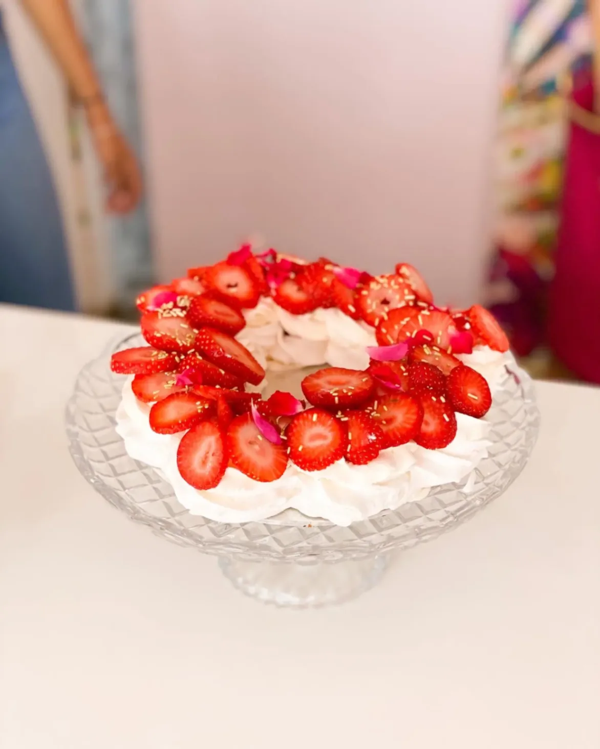 Pavlova garnie de fraises fraîches et de pétales de fleurs, présentée sur un présentoir en verre transparent