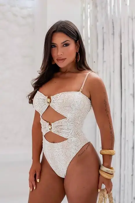 Femme portant un maillot une-pièce blanc ajouré avec détails dorés, posant en intérieur lumineux