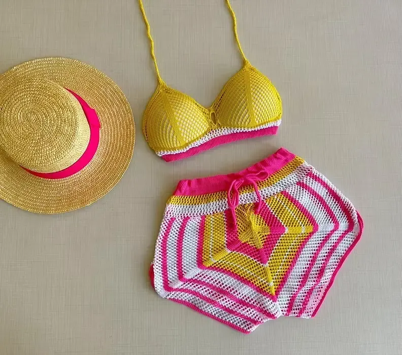 Ensemble bikini crochet jaune et rose avec un short assorti, posé à côté d’un chapeau de paille