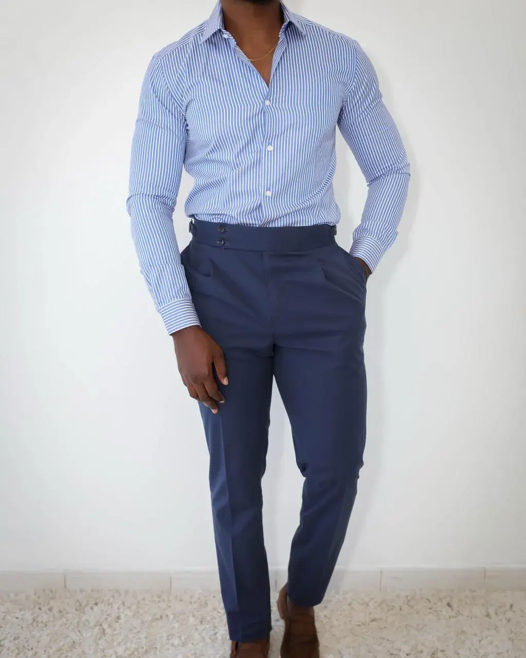 Homme portant une chemise à rayures bleues et un pantalon habillé bleu marine, look élégant et moderne devant un fond blanc.