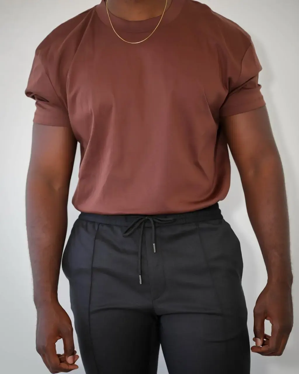 Homme portant un t-shirt marron et un pantalon noir taille élastique, style décontracté et moderne en studio