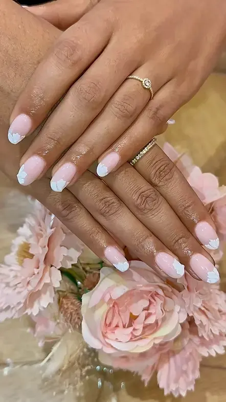 Mains avec manucure rose pâle et motifs blancs, posées sur un bouquet de fleurs dans une ambiance raffinée.