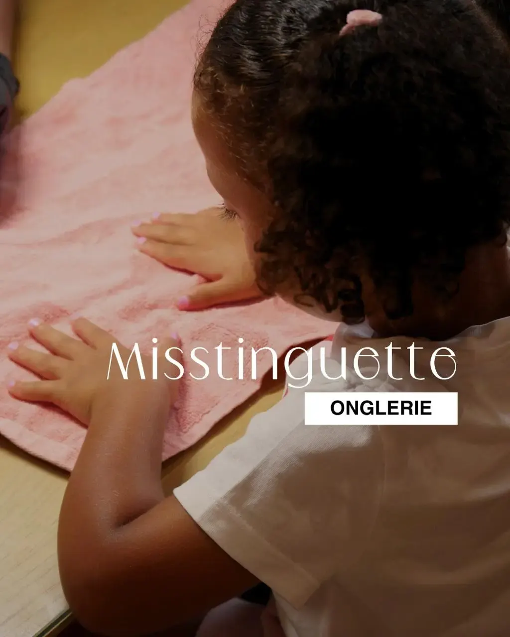 Enfant posant ses mains sur une serviette rose lors d’une séance de manucure dans un salon onglerie.