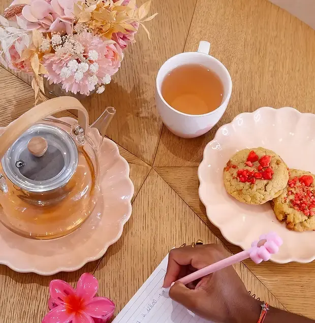 Tasse de thé, théière en verre et cookies aux fraises sur une table en bois, ambiance douce et florale.