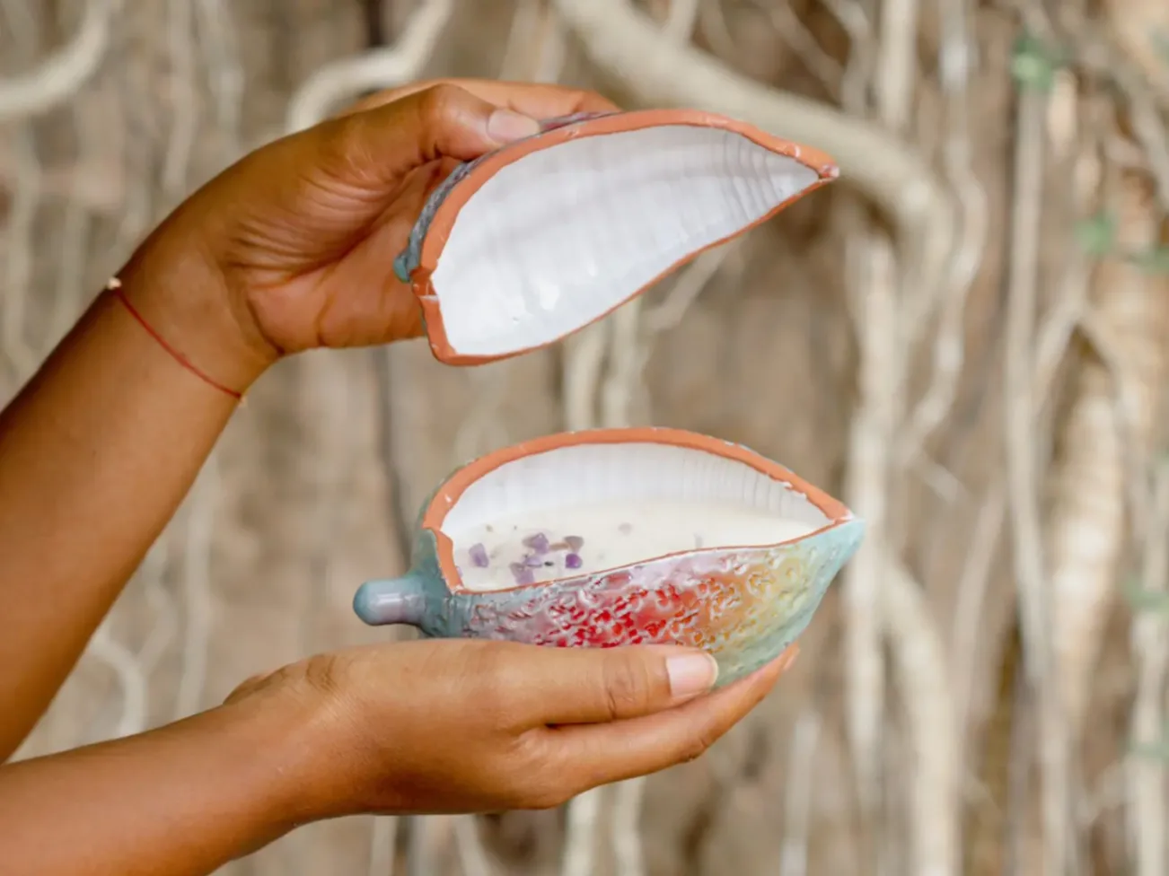 Photophore en céramique en forme de coquillage tenu entre deux mains, laissant apparaître l’intérieur avec une bougie parfumée et des cristaux
