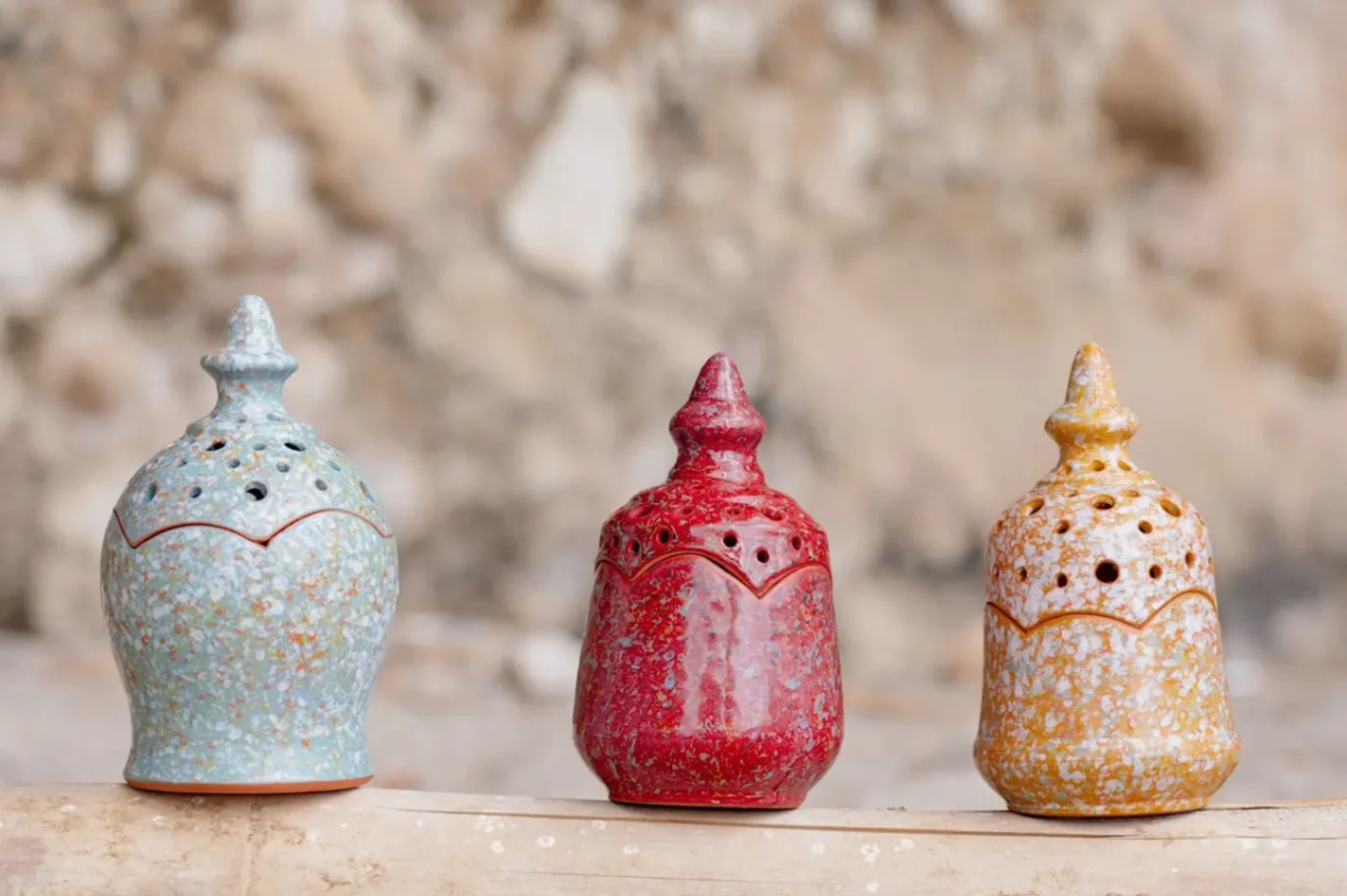 Photophores artisanaux en céramique colorée alignés sur un bois naturel, avec finitions texturées bleu, rouge et ocr