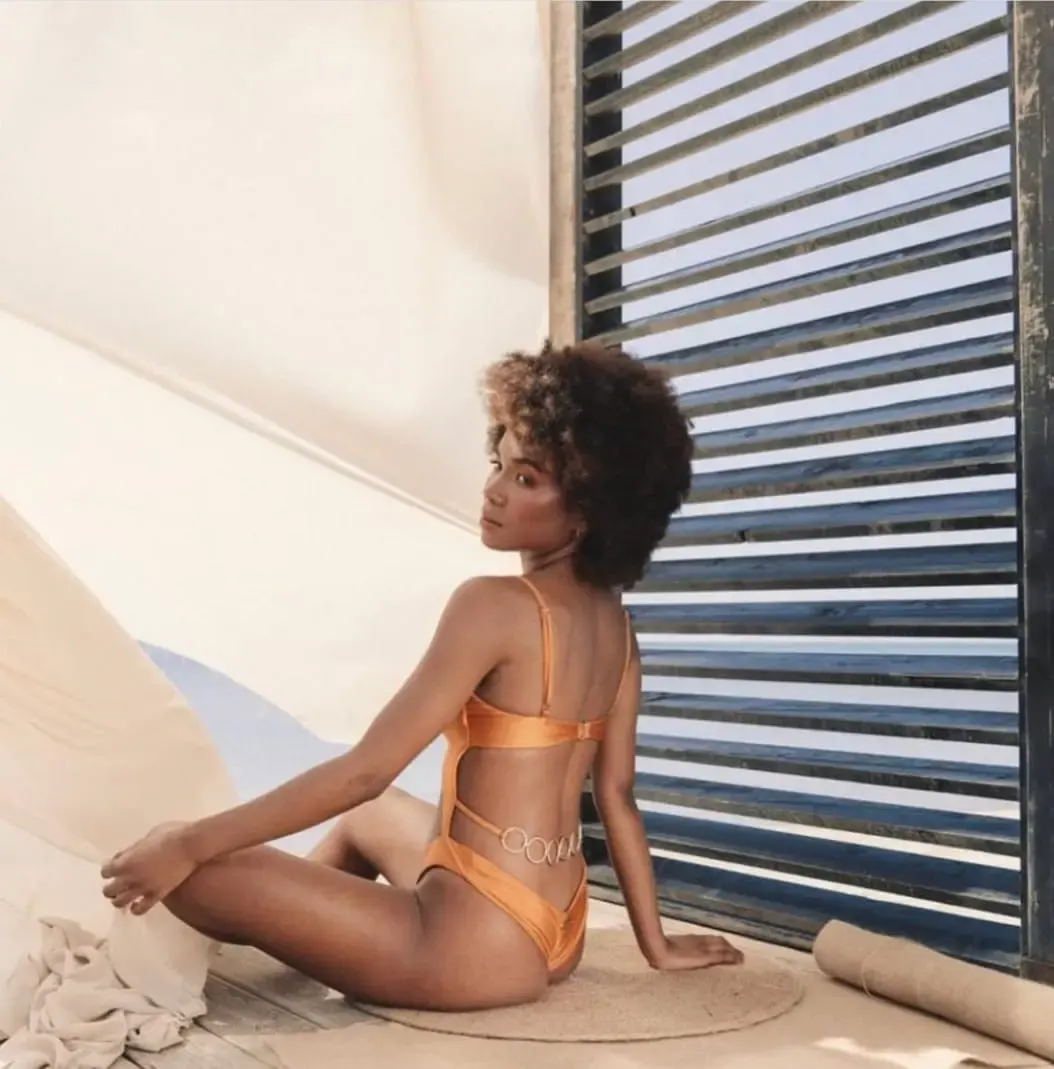 Femme portant un maillot de bain une-pièce orange ajouré avec anneaux métalliques, posant dans un décor lumineux