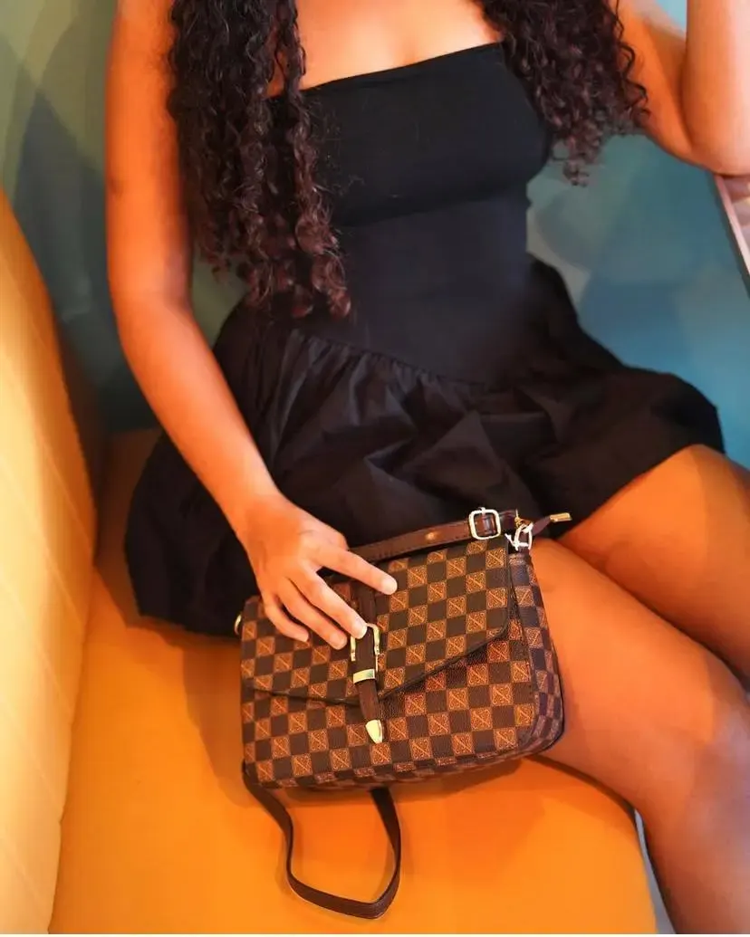 Femme portant une robe noire avec un sac à main marron motif damier posé sur ses genoux