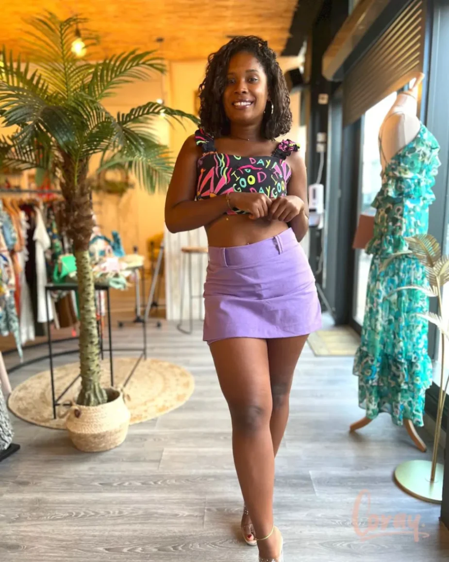 Jeune femme portant une jupe violette et un top graphique coloré dans la boutique Coray.