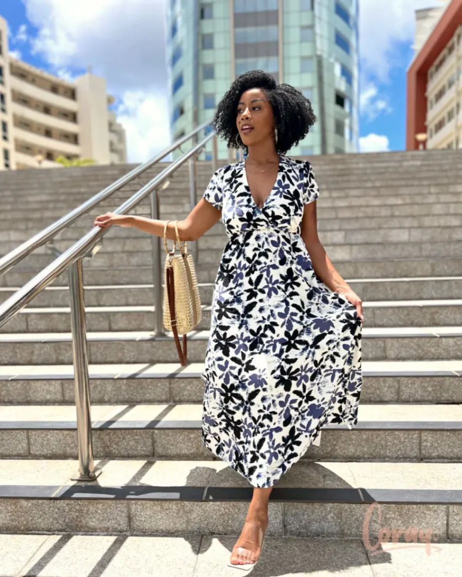 Femme élégante portant une robe midi fleurie noir et blanc posant sur un escalier urbain.
