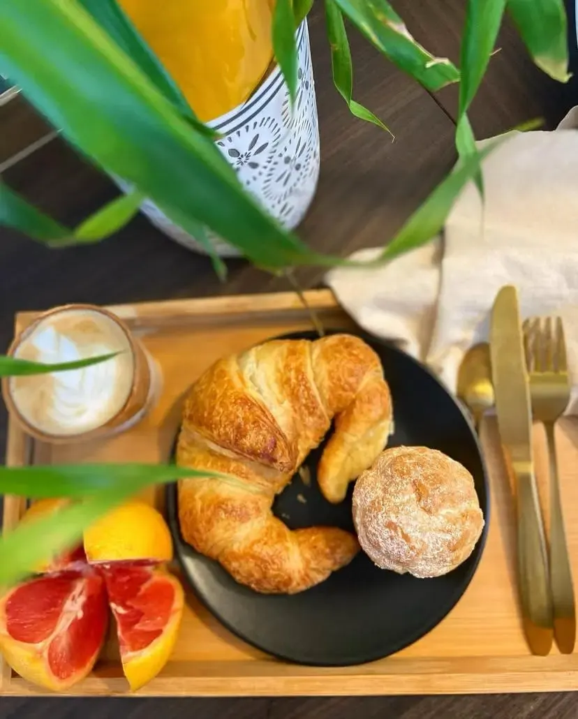 Petit-déjeuner gourmand avec croissant, muffin, café latte et pamplemousse servi sur un plateau en bois.