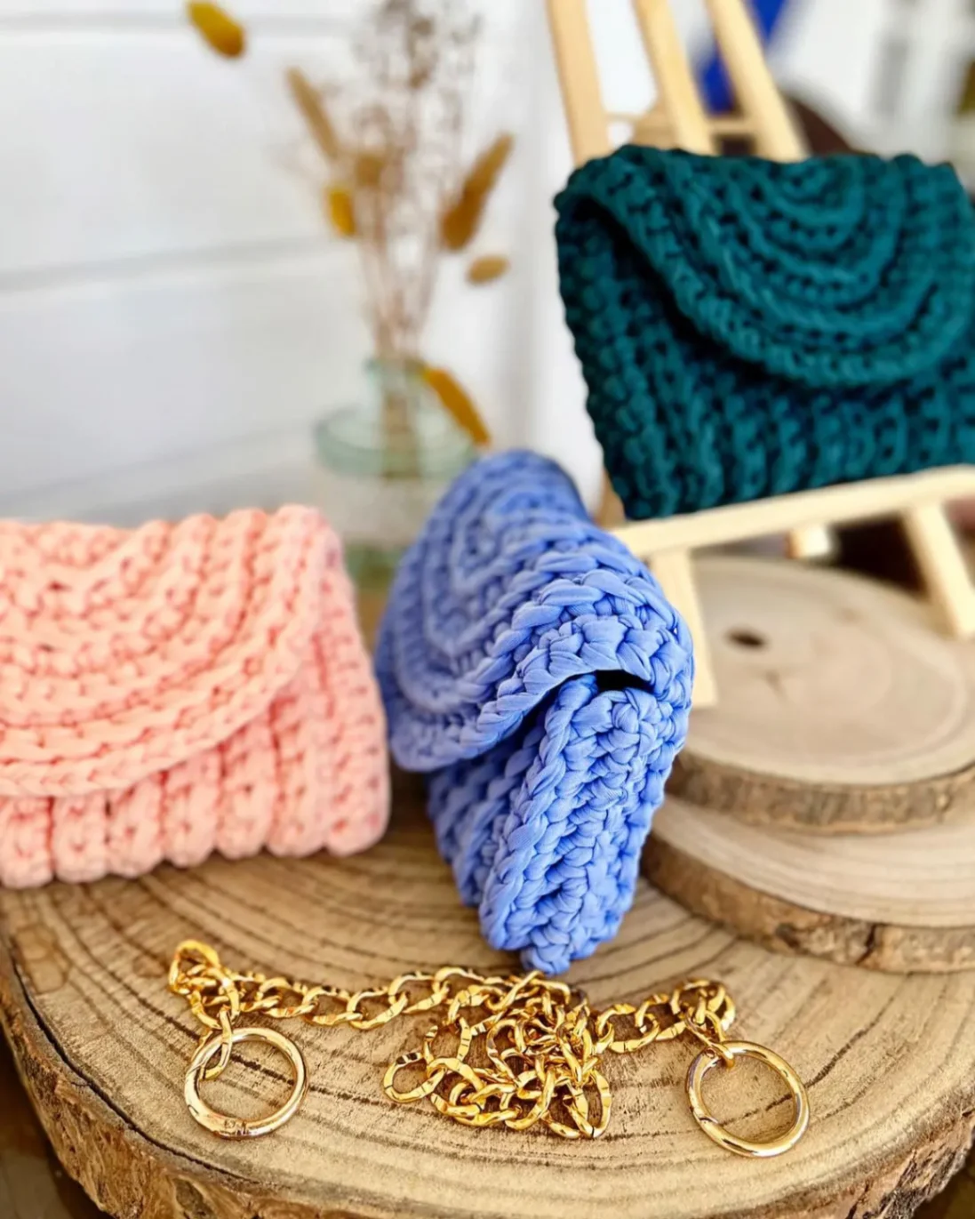 Ensemble de petits sacs en crochet pastel faits main, rose, bleu et vert, accompagnés d’une chaîne dorée.