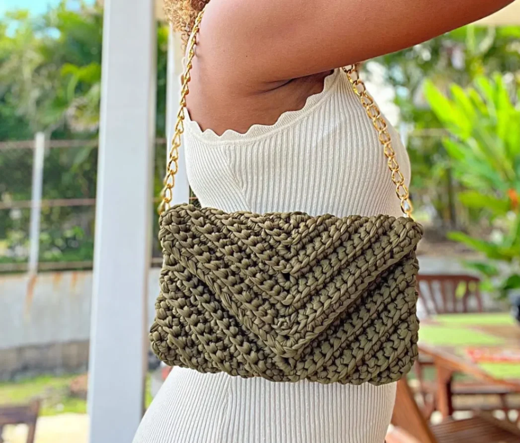Sac en crochet kaki porté à l’épaule avec bandoulière chaîne dorée – accessoire artisanal.