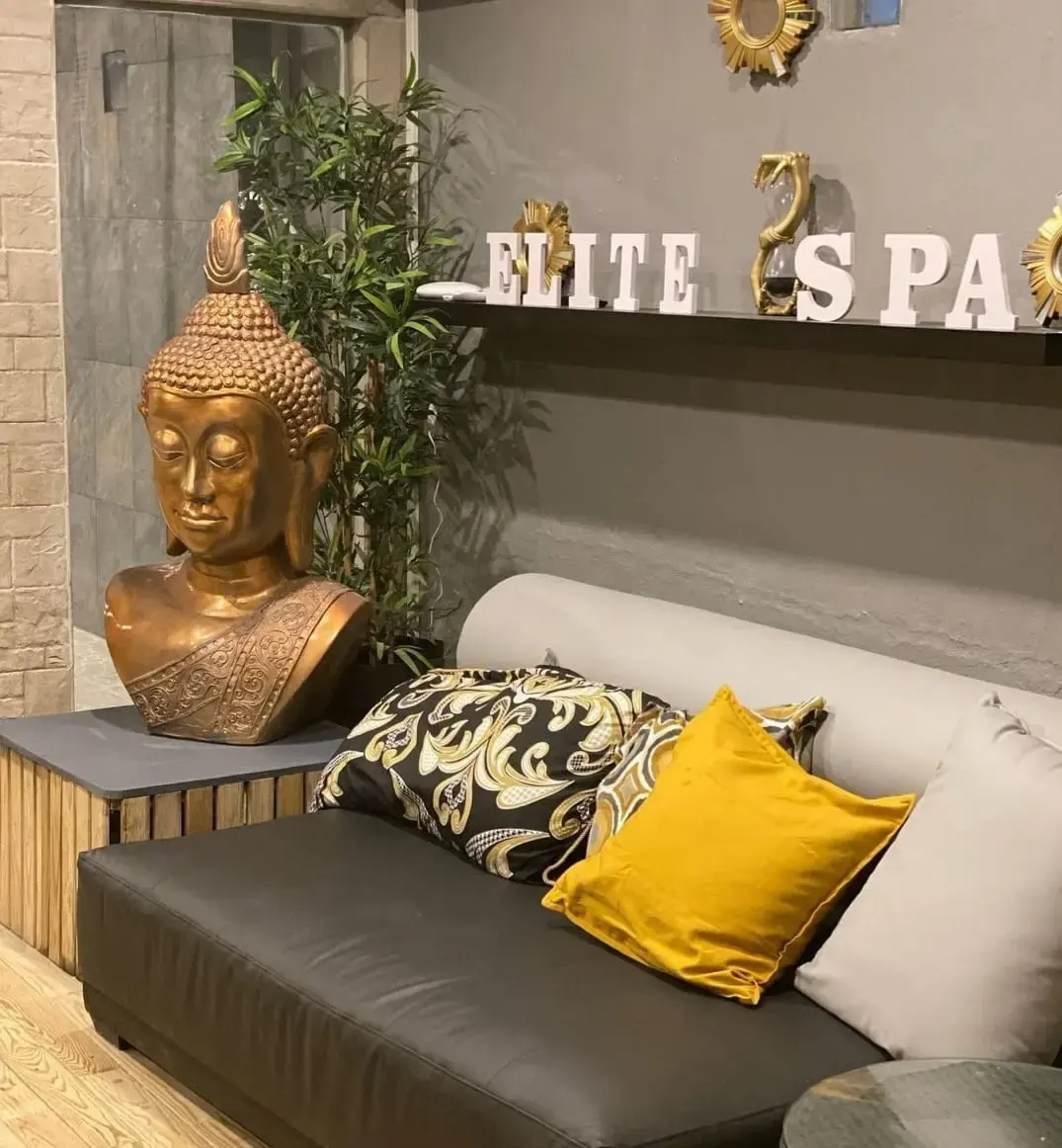 Espace détente d’Elite Spa avec statue de Bouddha dorée, canapé moderne et décoration zen.