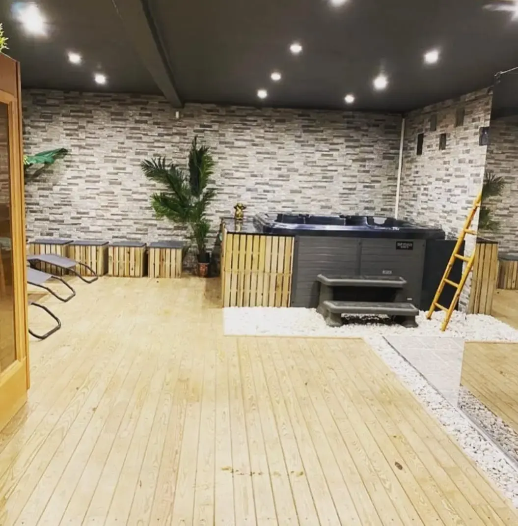 Grand espace de relaxation chez Elite Spa avec jacuzzi encastré et décoration bois et pierre.