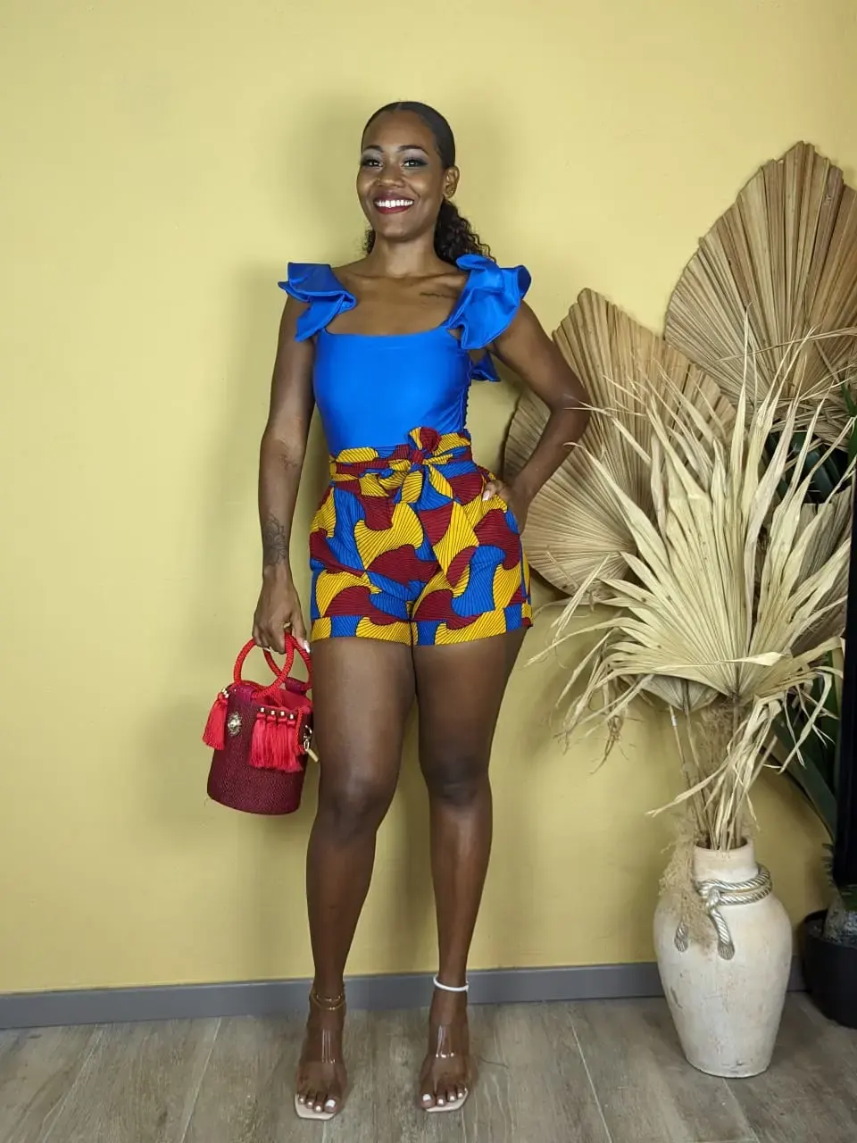 Femme portant un short wax coloré rouge jaune bleu avec un top bleu à volants, look estival et vibrant