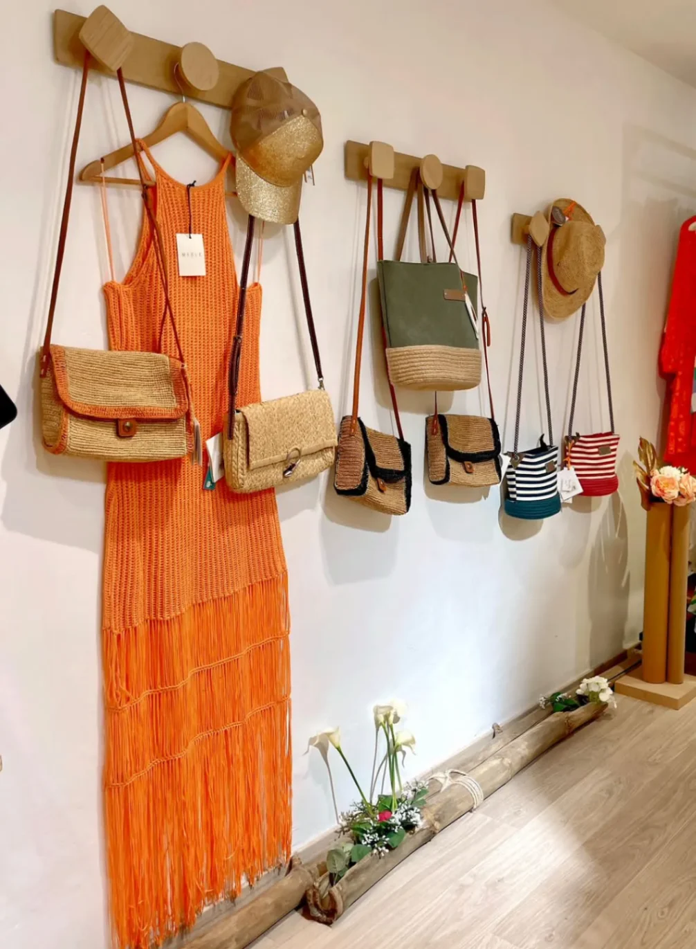 Sélection de sacs en raphia suspendus avec robe orange en maille dans une boutique de prêt-à-porter tropicale.