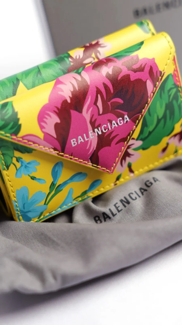 Porte-monnaie Balenciaga jaune à imprimé floral multicolore présenté sur un sac de protection en tissu.