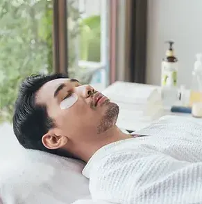 Homme allongé recevant un soin contour des yeux avec patchs hydratants.