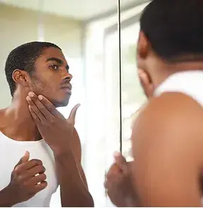 Homme observant de près la peau de son visage dans le miroir avant sa routine de soin