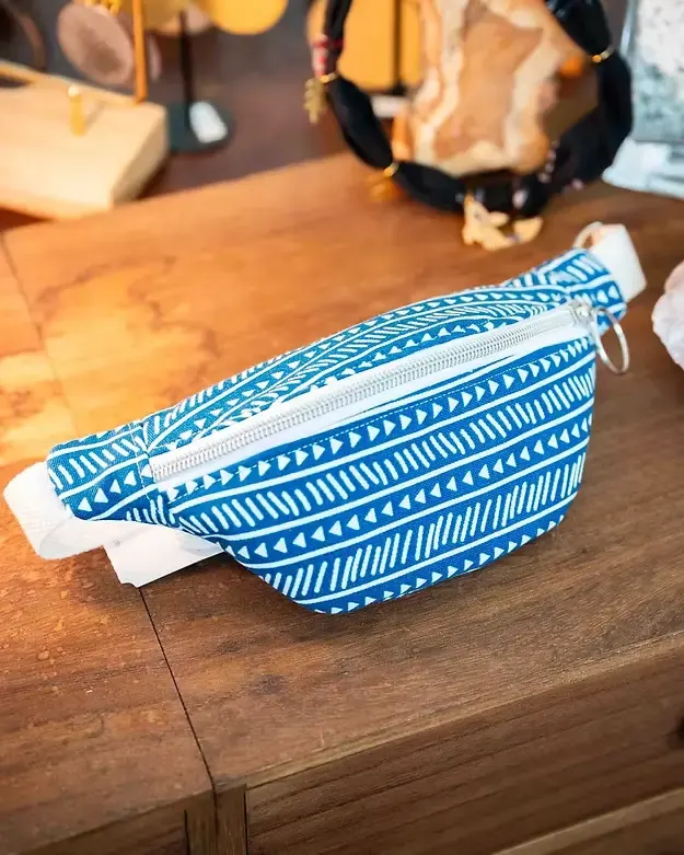 Sac banane bleu à motifs géométriques blancs posé sur un comptoir en bois dans une boutique artisanale.