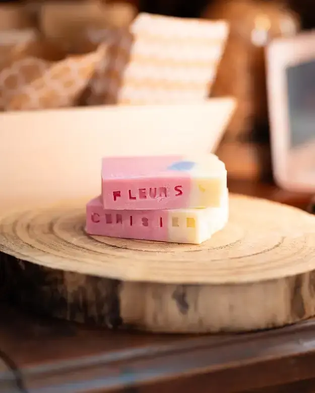 Savons artisanaux parfumés aux fleurs de cerisier, présentés sur une tranche de bois dans une boutique artisanale.