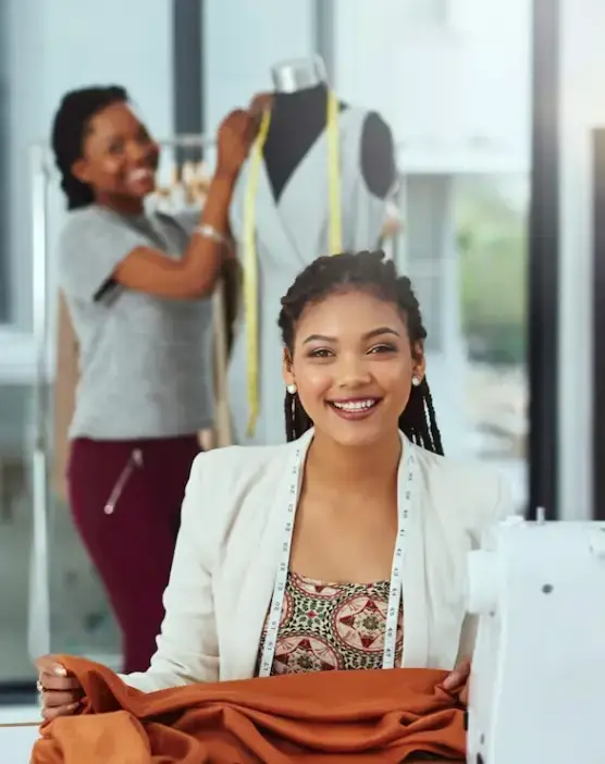 Jeune couturière souriante travaillant dans son atelier de couture en Martinique, tenant un tissu devant sa machine à coudre.