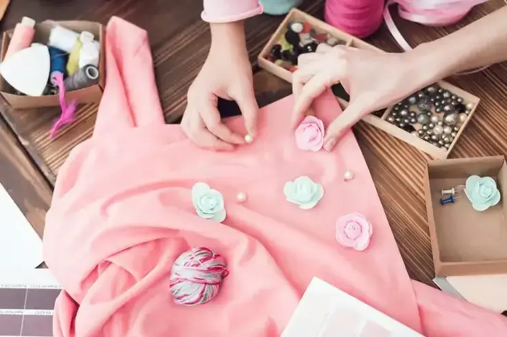 Mains ajoutant des fleurs décoratives et accessoires sur un tissu rose dans un atelier de couture