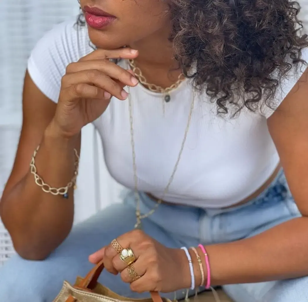 Femme portant plusieurs bijoux dorés, dont des bagues, bracelets et un collier, avec un style casual.