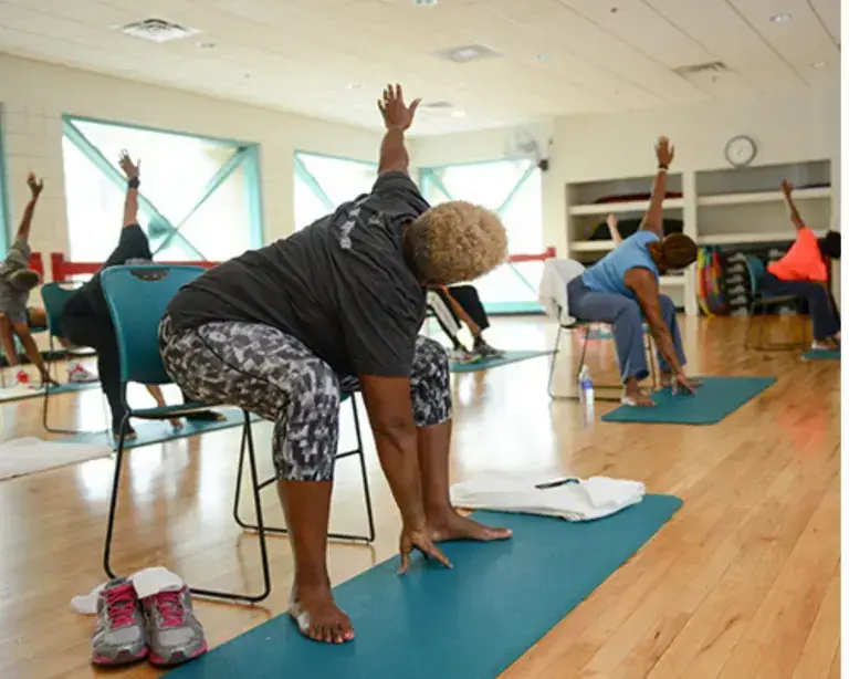 Groupe de femmes seniors pratiquant le yoga sur chaise dans une salle lumineuse.