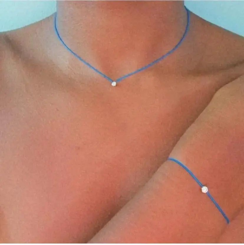 Collier et bracelet minimalistes en fil bleu avec petite perle, portés sur la peau.
