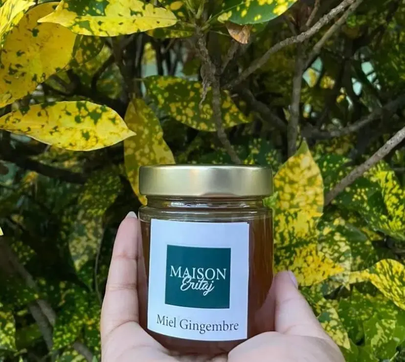 Pot de miel au gingembre Maison Eritaj tenu dans une main devant un feuillage tropical