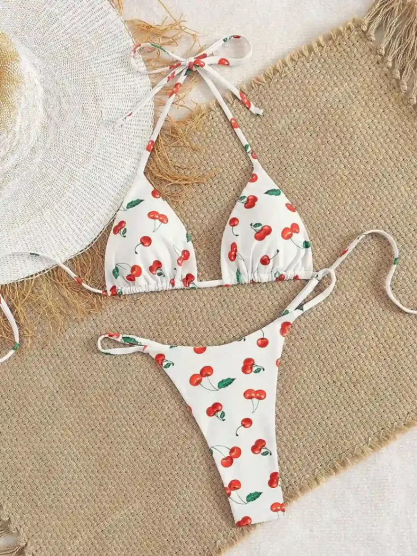 Bikini blanc deux pièces avec imprimé cerises posé sur une serviette estivale