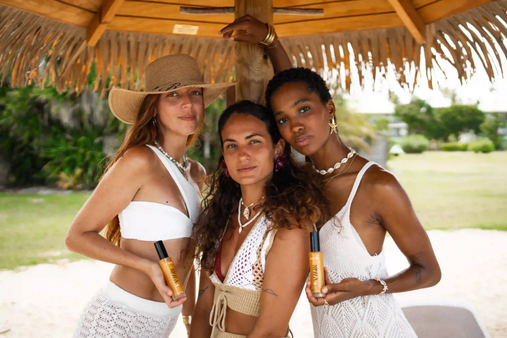 Trois femmes en tenues blanches posant sur la plage avec l’huile bronzante NIWA.