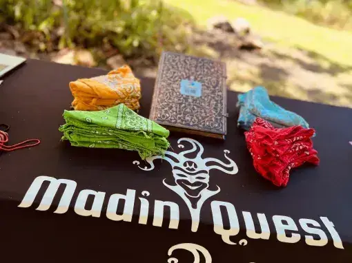 Table MadinQuest avec foulards de couleurs et carnet de jeu pour une aventure immersive.