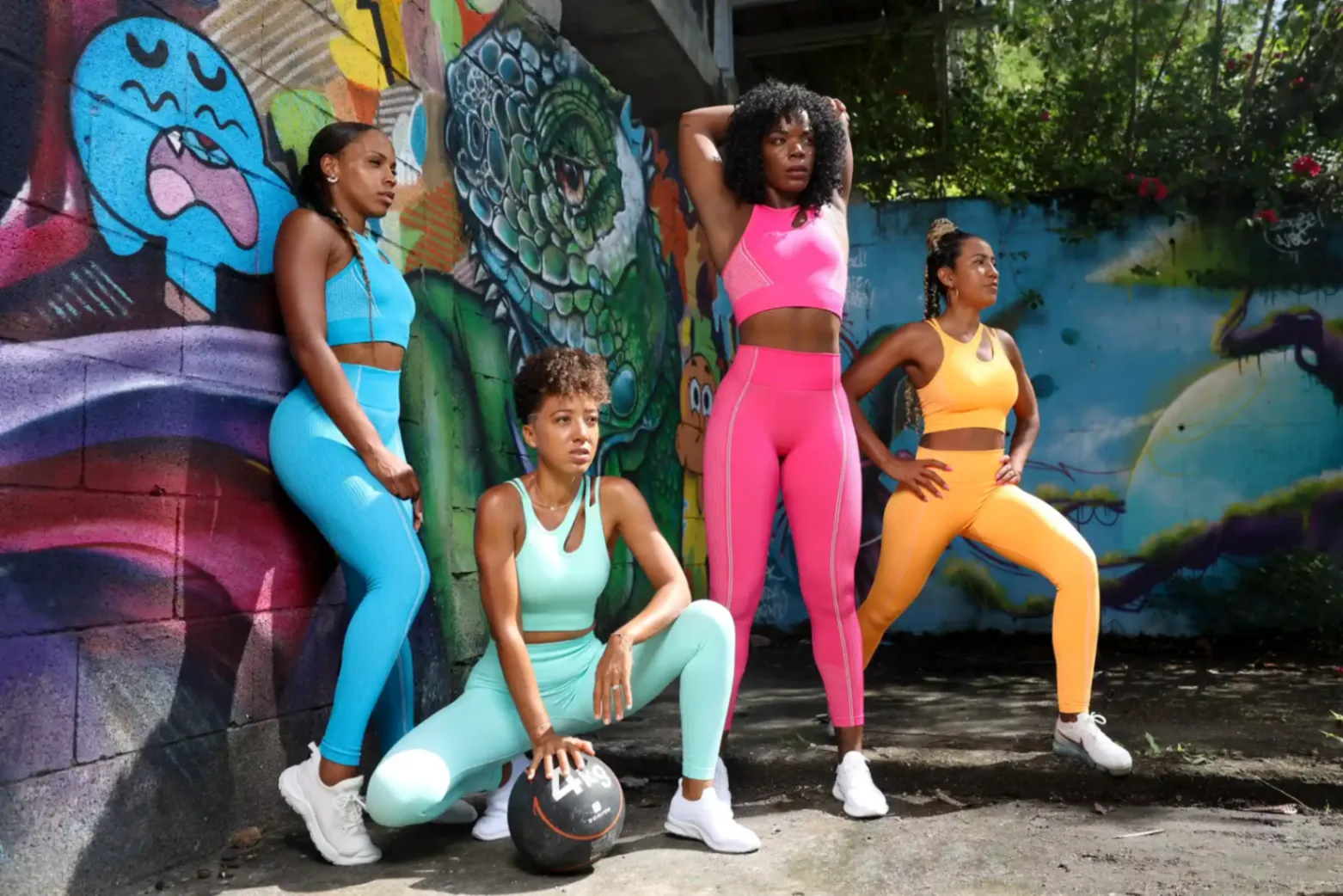 Groupe de femmes en tenue de sport colorée posant devant un mur graffiti pour une séance fitness.