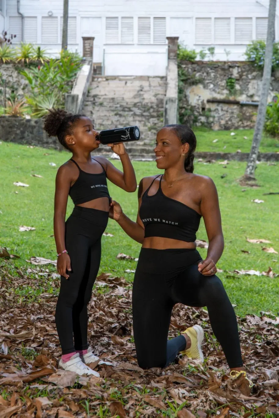 Mère et fille en tenue de sport noire s’entraînant en plein air dans un parc.