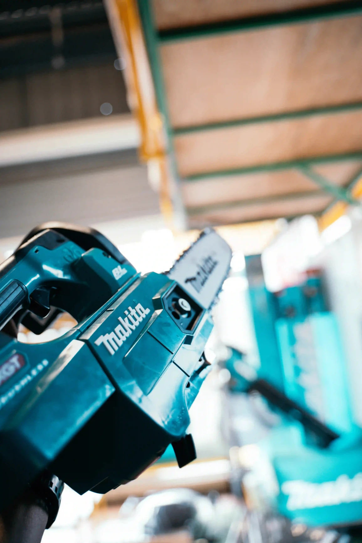 Gros plan sur une tronçonneuse Makita turquoise dans un atelier, montrant la marque et les détails de l’outil.