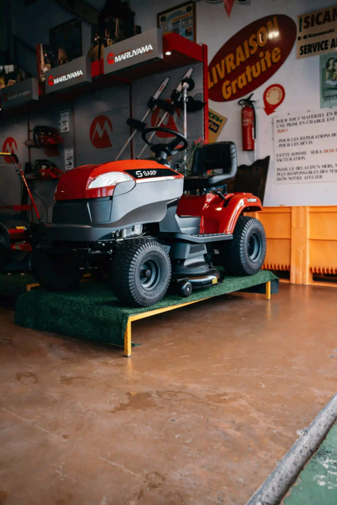 Tondeuse autoportée rouge de la marque SARP exposée dans un magasin de matériel de jardinage.
