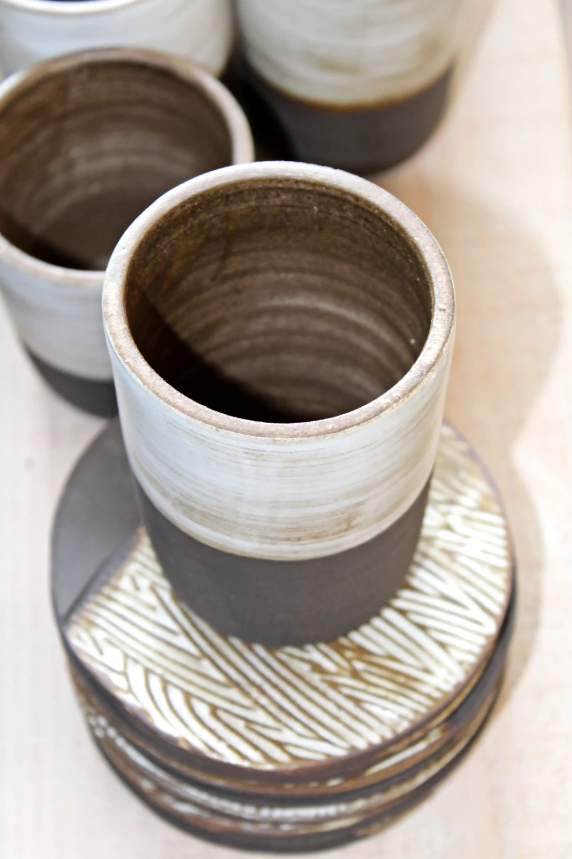 Gobelet artisanal en céramique aux tons bruts et blancs, posé sur un plateau texturé.