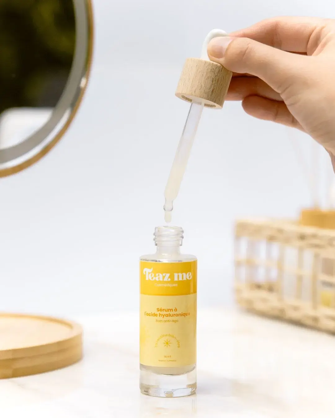 Main tenant une pipette laissant tomber une goutte du sérum à l’acide hyaluronique Teaz Me dans son flacon.