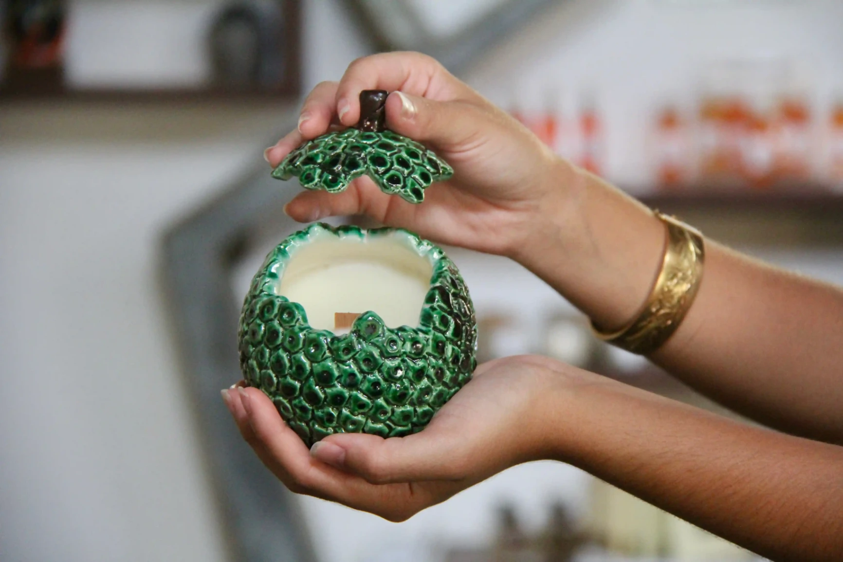 Bougie en céramique artisanale en forme de fruit à pain vert, tenue dans les mains, couvercle ouvert