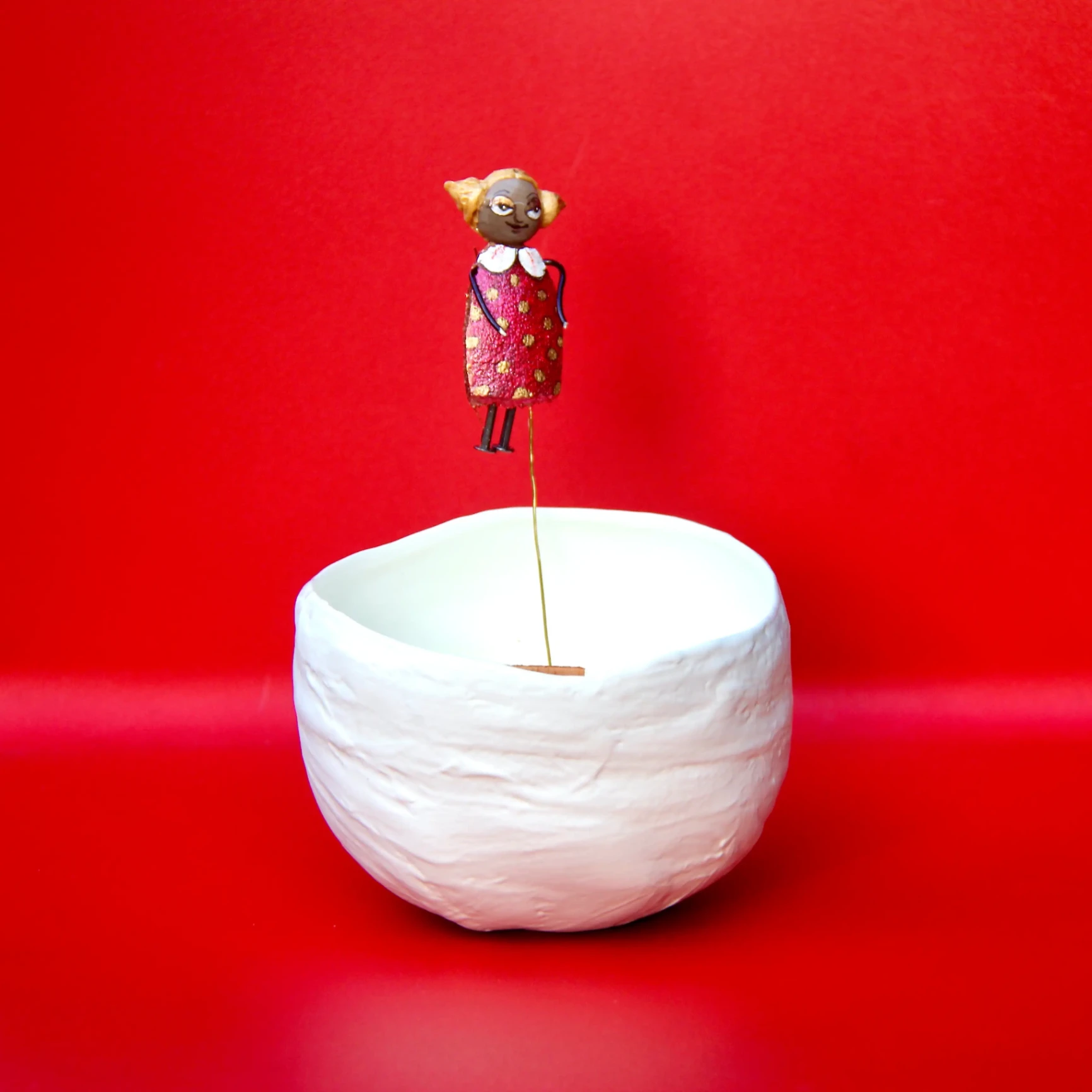 Bol en céramique blanche avec une petite figurine artisanale colorée sur fond rouge vif